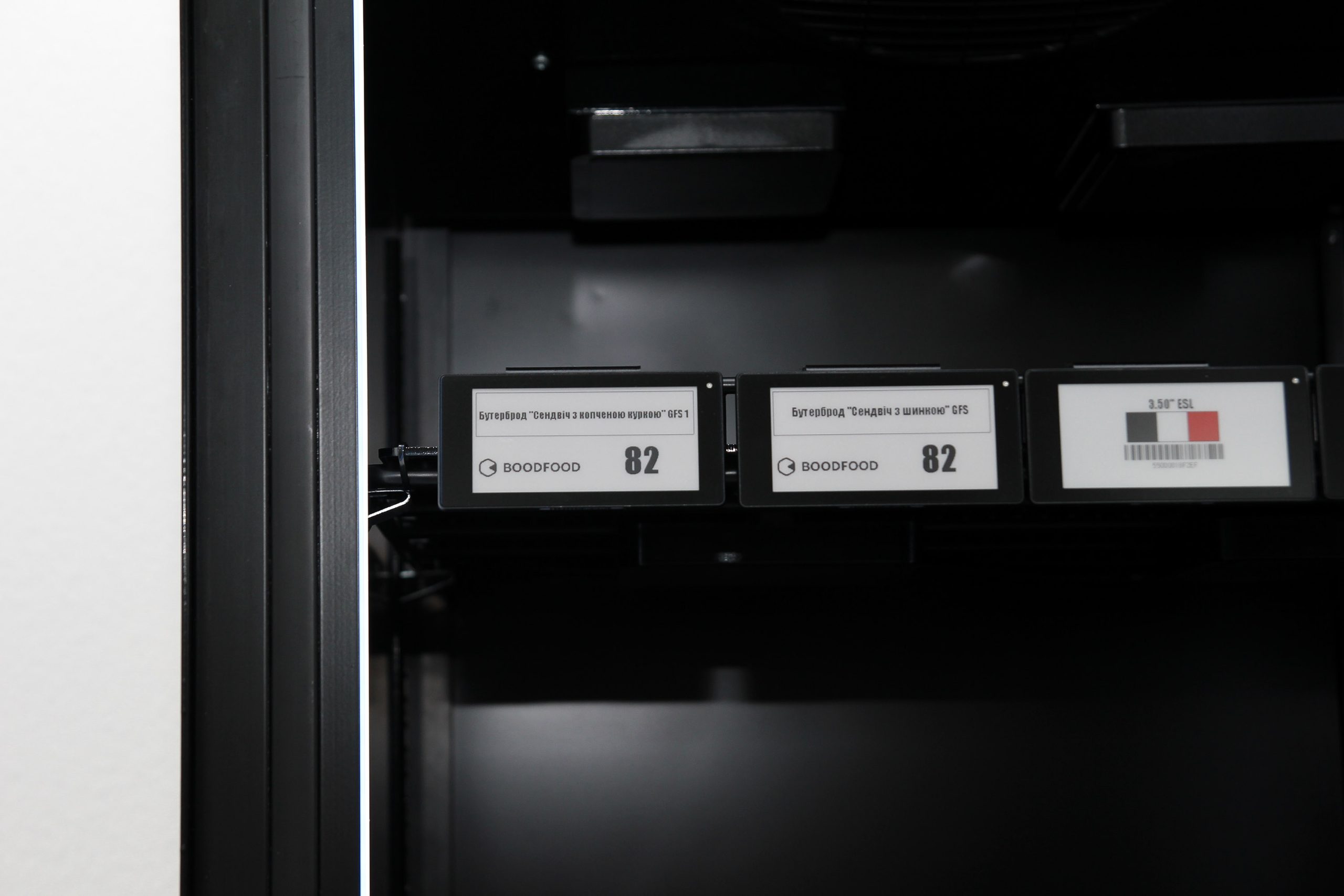 Electronic shelf labels on the front edge of an empty shelf inside a cabinet
