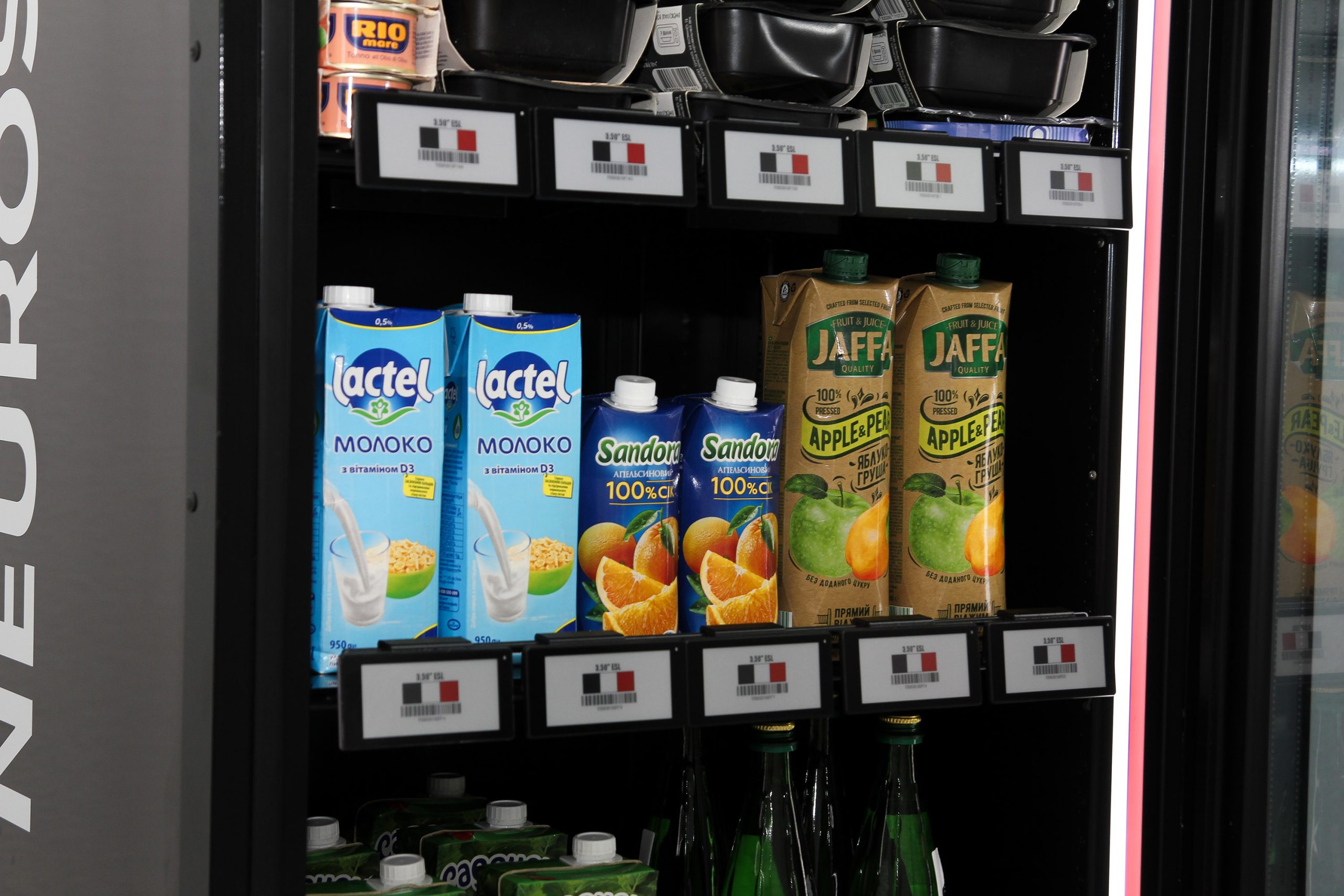 Shelves of an open cabinet with milk and juice cartons, electronic shelf labels along the shelf edges