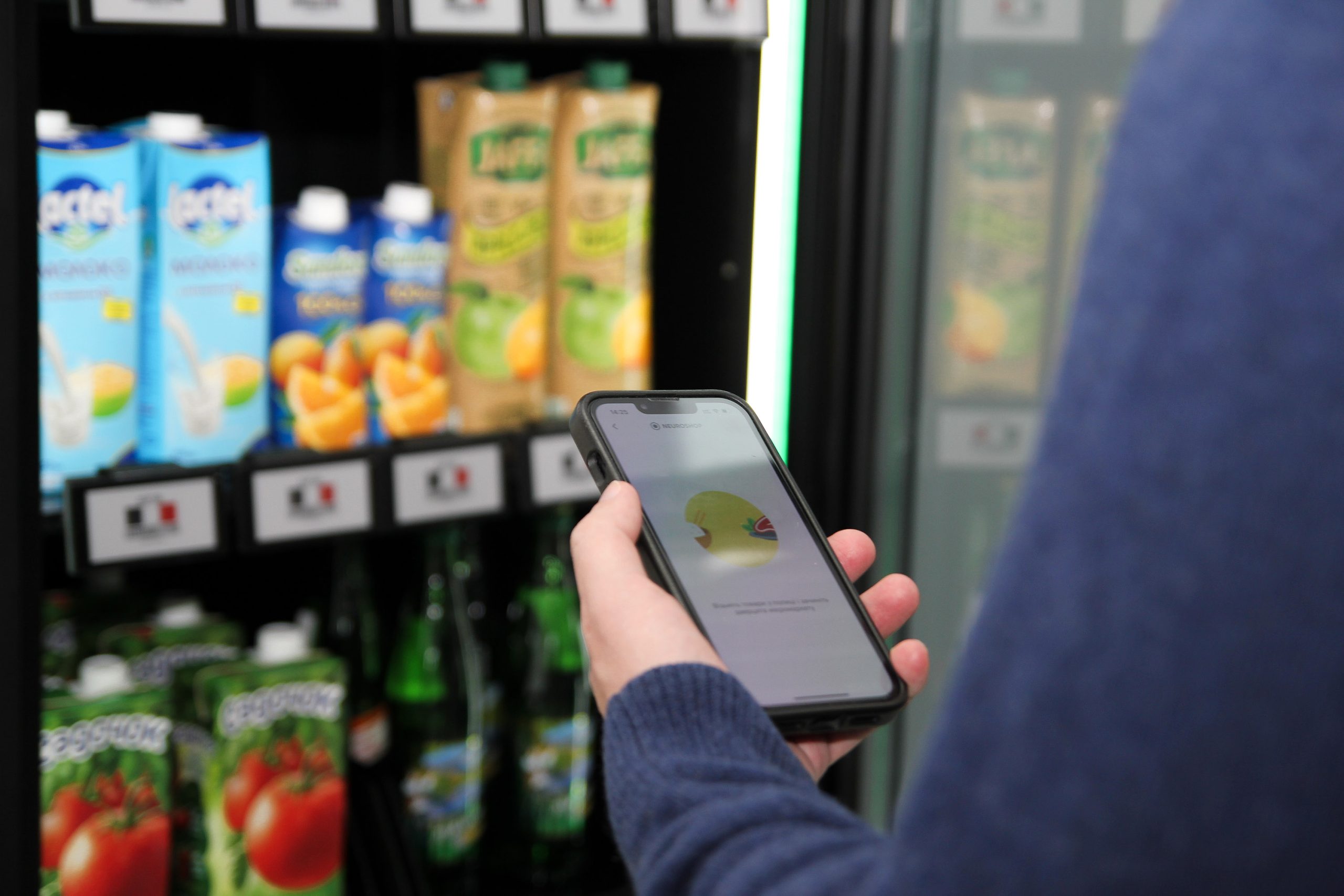 Hand holding a phone by the open shelves of a cabinet, juice and milk drinks in cartons on the shelves