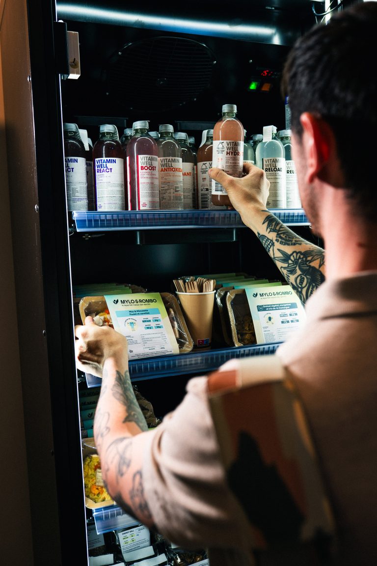 Man taking a bottle from the top shelf of an open lit cabinet